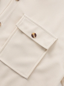 Detailed macro view of cream waffle knit fabric with pocket and tortoiseshell button