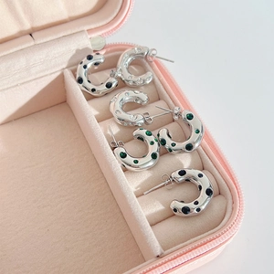 Macro view of C-shaped silver earrings with colorful stones on pink velvet
