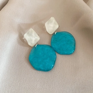 Macro shot of geometric acrylic earrings with marble texture and lake blue pendants