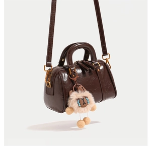 Detail of a brown Boston bag with smooth leather texture and a plush alpaca keychain