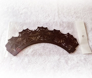 Flat lay of laser-cut spider web cupcake wrappers in black packaging on white plush background