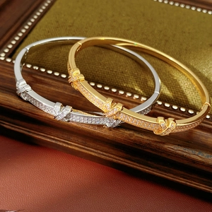 Detail of 18k gold and silver X-shaped bangles with pavé zircon stones on green velvet