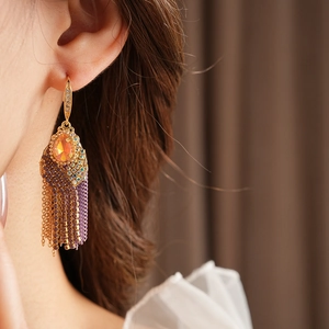 Detail view of gold tassel earrings with orange stones and purple beads worn by a model