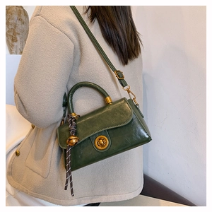 Detail of dark green vintage oil wax leather handbag with golden lock and bell charm