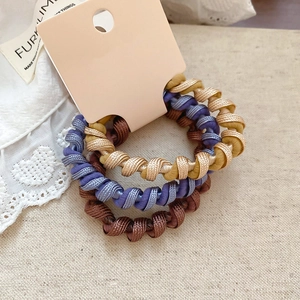 Gros plan de trois élastiques à cheveux spirales en doré, bleu et marron sur lin