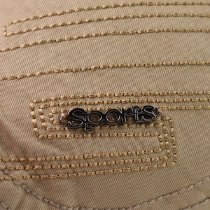 Detail view of khaki cotton fabric with decorative stitching and metal SPORTS logo