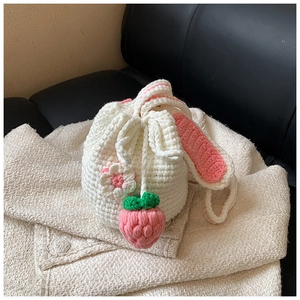 Detail of handmade knit bunny bucket bag with strawberry charm on a cozy surface