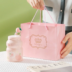 Pink peach shaped ceramic mug with straw and matching gift bag on a white table