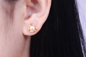 Detailed view of geometric gold triangle stud earrings with pink freshwater pearls