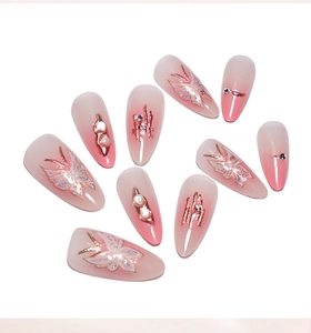 Detail of almond press-on nails with pink ombre, butterfly charms and pearl accents