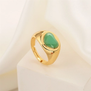 Macro shot of gold wide band ring with green heart inlay on white silk background