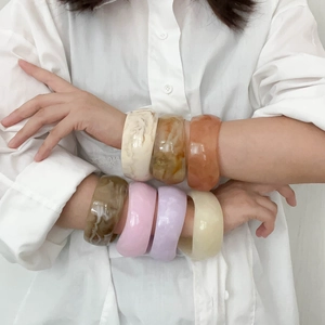 Wide irregular resin bangles in multiple colors shown on a model's arm for a retro look