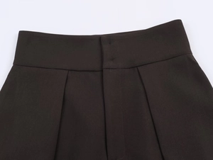 Detail of high-waist dark brown trousers showing waist tailoring and zipper fly stitching