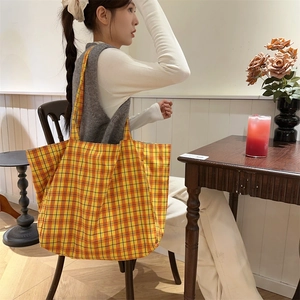 Close-up of a large capacity orange plaid canvas tote bag used in a cozy cafe setting