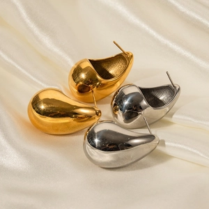 Polished gold and silver teardrop earrings displayed on elegant white silk fabric
