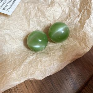 Detailed view of green spherical stud earrings with cat-eye luster on vintage paper