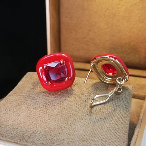 Macro detail of red square candy earrings with zircon stones on a beige jewelry cushion