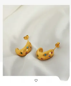 Detail of thick gold C-shaped earrings with colorful gemstones and star-shaped grooves