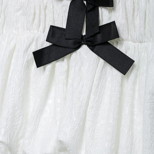 Blouse blanche sans manches à col en V avec détail nœud noir et texture plissée chic