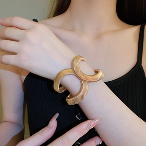 Close-up of golden crossover spring bracelet with vertical textured metallic patterns