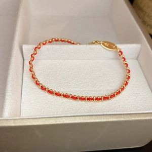Detail of red braided bracelet with gold beads and engraved oval charm in a white box