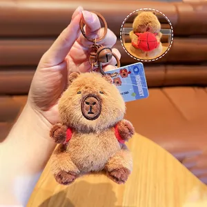 Close-up of brown capybara plush keychain with red backpack and metal bell detail