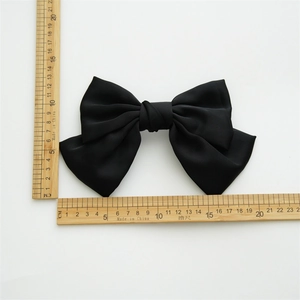Large black satin fabric bow hair clip shown with a ruler for size measurement on white background
