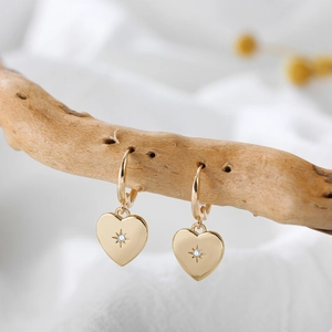 Detail of 18K gold heart earrings with star-set diamond on natural wooden branch