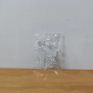 Macro detail of a clear acrylic snowflake ornament in packaging with silver ribbon
