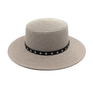 Gros plan d'un chapeau de paille beige avec ruban noir orné de clous argentés