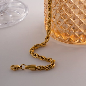 Détail d'un collier chaîne torsadée dorée avec fermoir mousqueton sur une surface blanche