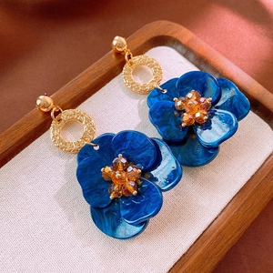 Detailed view of blue floral earrings with gold geometric rings and orange crystal beads