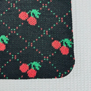 Close-up detail of knitted fabric showing red cherry patterns on black texture