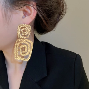 Detailed view of large golden geometric spiral earrings with textured finish on model
