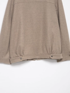 Close-up of the hem detail and hem strap on a tan wool bomber jacket with fine texture
