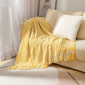 Hand-knitted yellow and white striped chenille blanket with decorative tassels on a sofa