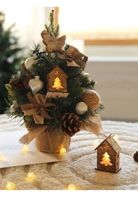 Mini Christmas tree with warm LED lights and wooden cottage on a plush white surface