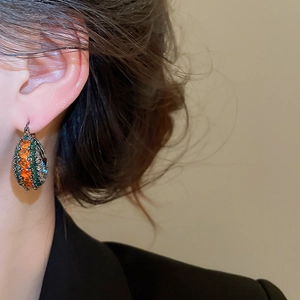 Nahaufnahme von Vintage-Ohrringen mit orangefarbenen und grünen Steinen am Model