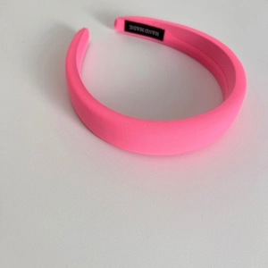 Detail of neon pink fabric headband featuring thick padded design and handmade label