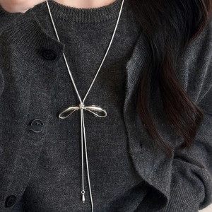 Silver bow pendant necklace with long tassel design on a dark knit cardigan