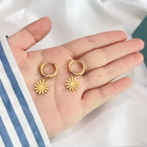 Detailed close-up of golden daisy pendant earrings held by hand on white fabric background