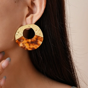 Detail of large gold hammered metal and tortoise shell resin open hoop earrings on a model