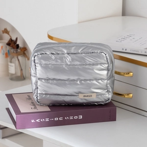 Close-up of a silver quilted makeup bag with puff design and JIMEIZI label on books