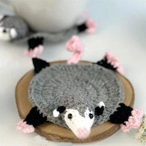 Handmade crochet opossum coaster detail showing gray yarn texture and spiral tail