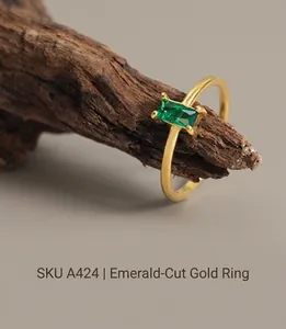 Detailed close-up of a gold-plated open ring with a rectangular green emerald gemstone
