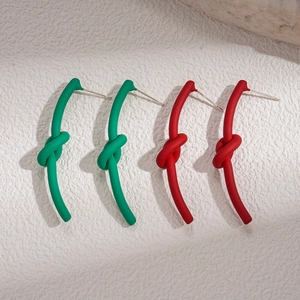 Orecchini a nodo minimalisti in rosso e verde opaco su sfondo di pietra bianca