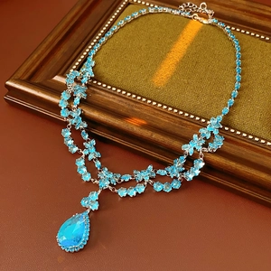 Détail d'un collier argenté avec pierres bleues en fleur et pendentif goutte d'eau