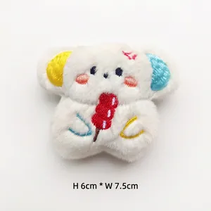 Detail view of 6x7.5cm plush white bear brooch with embroidered snack and blue-yellow ears