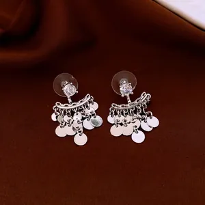 Silver-toned zircon stud earrings with fan-shaped metal disc tassels on silk background