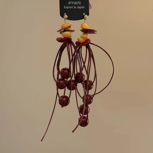 Detail of red tassel drop earrings with dark red beads and golden ear studs on card